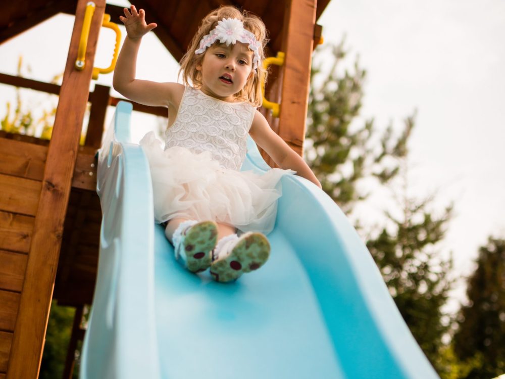 Little girl in white dress afraid as she slides down
