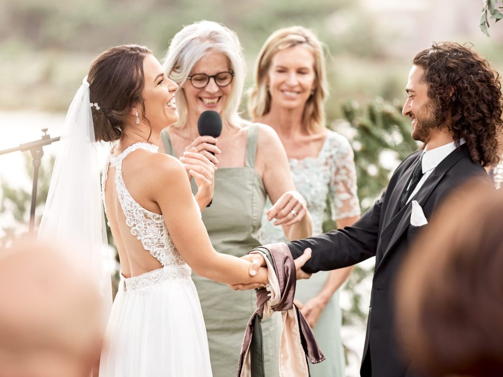 Mother at a wedding doing a speech for bride and groom, smiling and laughing together. Wedding official, celebration and love with family at the ceremony outdoors. Marriage, romance and happy couple